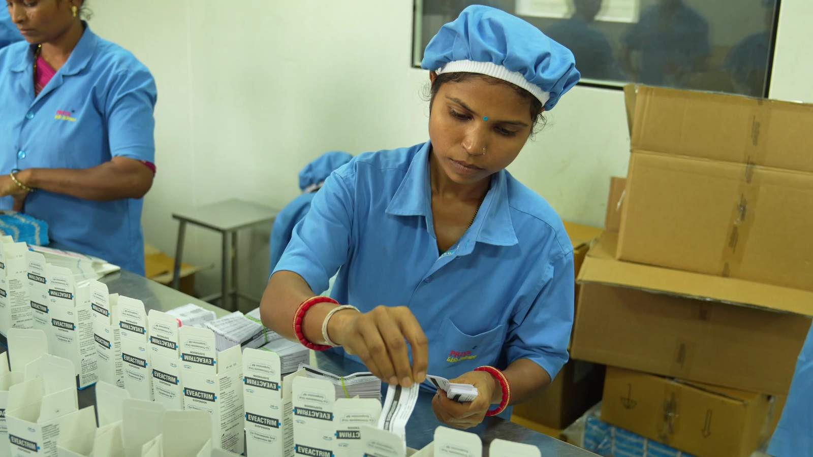 Packing staff in blue uniforms assembling product cartons at the Priya Life Science facility